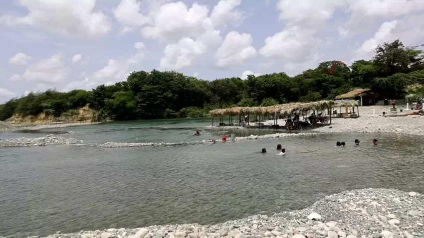 Pizarrete, Peravia. — Enclavado entre gravas, granceras y los márgenes del río Nizao, se encuentra el balneario Los 3 Charquitos, nombrado así por los tres principales charcos que lo conforman, aunque hay otros cuerpos de agua en sus alrededores. Todos ellos son producto de las huellas que ha dejado la extracción de agregados para la industria de la construcción en esta parte del afluente. Este hermoso paraje, situado en la comunidad Los Polanco, en el distrito municipal de Pizarrete del municipio Nizao, provincia Peravia, se ha convertido en uno de los destinos favoritos del momento. Según residentes, el lugar ganó notoriedad tras la visita de figuras del mundo artístico y mediático, como La Insuperable, el Dotol Nastra y Miguel Céspedes, entre otros. Cada día, visitantes de distintas regiones del país acuden a disfrutar de sus aguas cristalinas y refrescantes, siendo los días de mayor afluencia los fines de semana largos, entre viernes y lunes, así como los días feriados. ¿Cómo llegar a Los 3 Charquitos? Desde Santo Domingo, el trayecto dura aproximadamente una hora. La ruta más utilizada es la misma que conduce a La Neverita. También te puede interesar: Al transitar por la carretera Sánchez —entre Baní y San Cristóbal— se gira a la derecha justo antes de cruzar el puente Lucas Díaz sobre el río Nizao, el cual marca el límite entre ambas provincias. Primero se llega a La Neverita y desde ese punto, Los 3 Charquitos se encuentra a unos 10 o 15 minutos, dependiendo del medio de transporte y la velocidad.